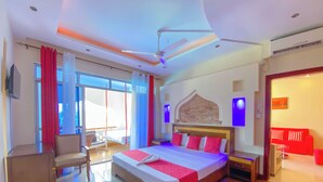 A spacious hotel room with a large bed, a desk, a chair, and a balcony with red curtains. - Shanzu Palm Beachfront Apartments (Mombasa)