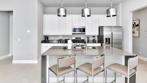 Uma cozinha moderna com eletrodomésticos de aço inoxidável, uma ilha central com banquetas e iluminação pendente.
