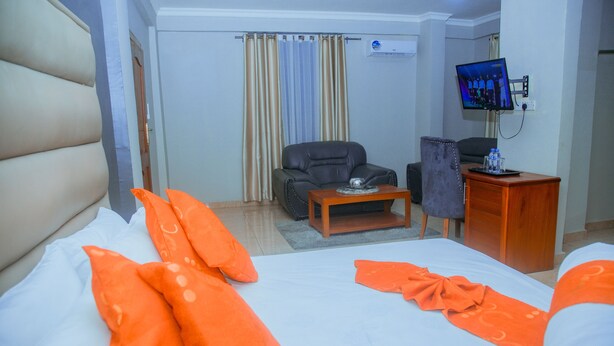 A hotel room with a large bed, a desk, a chair, a television, and a curtain. - LE GRAND MARIE HOTEL (Dar es Salaam)