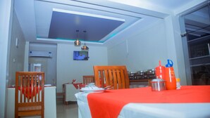 A dining area with a red tablecloth, wooden chairs, and a television mounted on the wall. - LE GRAND MARIE HOTEL (Dar es Salaam)