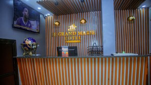 A reception desk with a striped wooden backdrop, a television mounted above it, and a sign reading "Le Grand Marie Hotel". - LE GRAND MARIE HOTEL (Dar es Salaam)