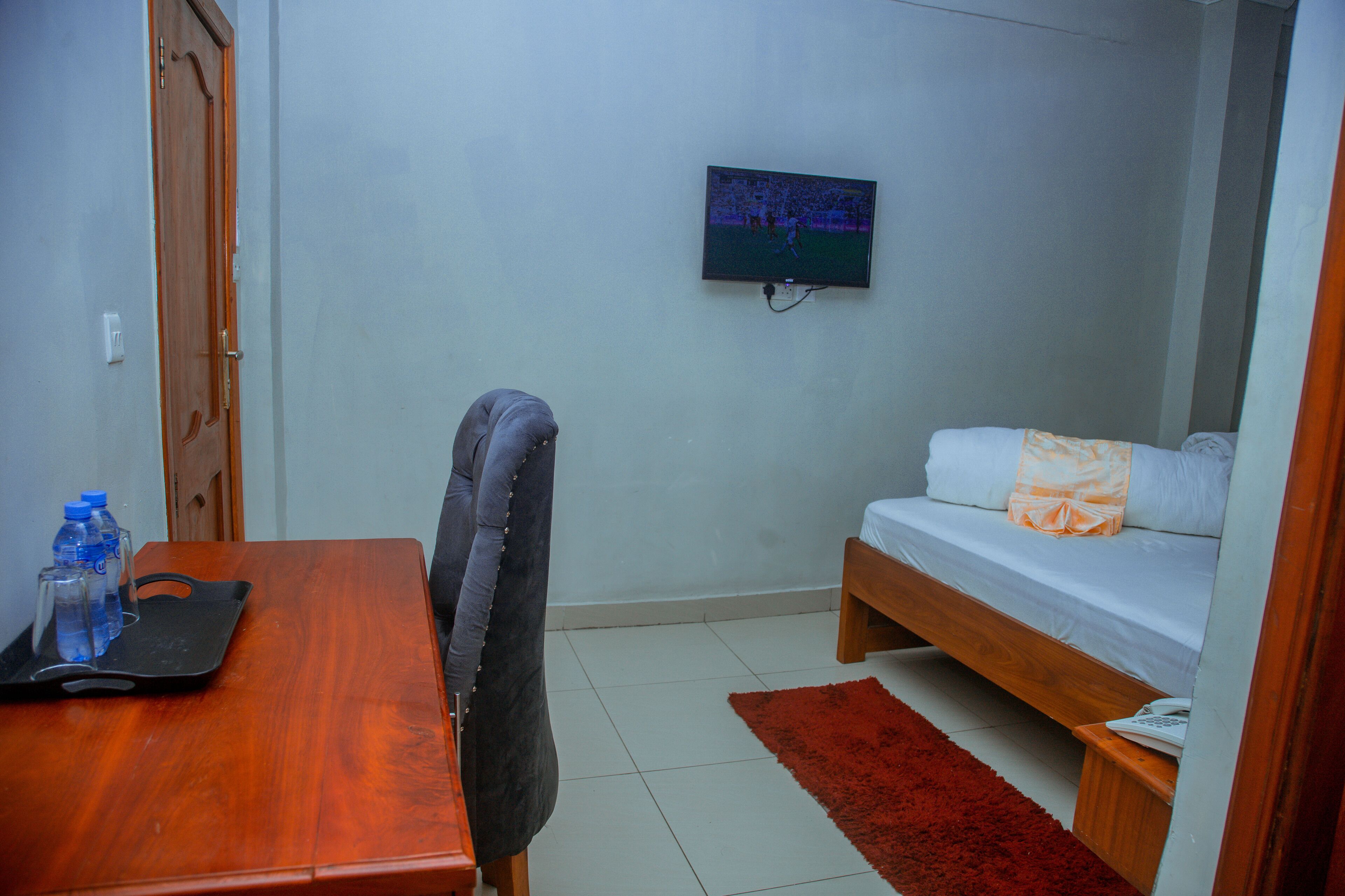 Una habitación pequeña con un escritorio de madera, una silla, una cama con una alfombra roja y un televisor en la pared.