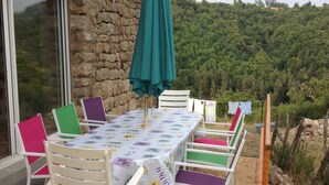 A stone building with a table and chairs set outside, overlooking a forested hillside.