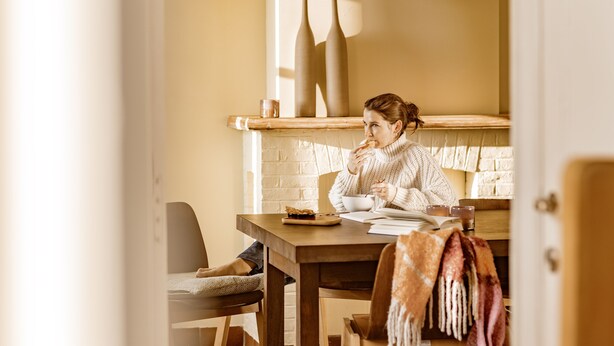 A person sitting at a wooden table with a book and a cup, in a room with a brick wall and a shelf with vases. - Ontdek de Kracht van de Rust, Dichtbij de Kust! (Veurne)