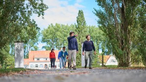 A pathway with a stone structure on the left, surrounded by trees and buildings in the background. - Ontdek de Kracht van de Rust, Dichtbij de Kust! (Veurne)