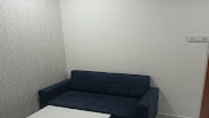 Une petite pièce au mobilier minimaliste, avec un seul canapé bleu, une petite table blanche et un mur blanc uni.