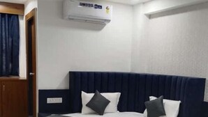 Une chambre d’hôtel avec un lit rond, une tête de lit bleu foncé, du linge de lit blanc et un ventilateur de plafond.