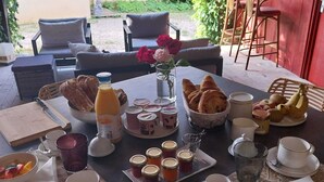 Ein Frühstückstisch mit verschiedenen Speisen und Getränken, umgeben von Sitzgelegenheiten im Freien.