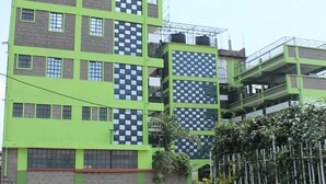 A multi-story building with a green facade and a checkered pattern on some windows. - ELAND ACCOMMODATIONS (Ongata Rongai)