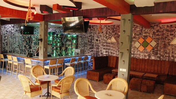 A bar area with a television, bar counter, and seating with wicker chairs and ottomans. - ELAND ACCOMMODATIONS (Ongata Rongai)