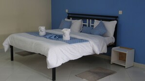 A neatly made bed with white bedding and blue accents, a bedside table, and a small nightstand. - ELAND ACCOMMODATIONS (Ongata Rongai)