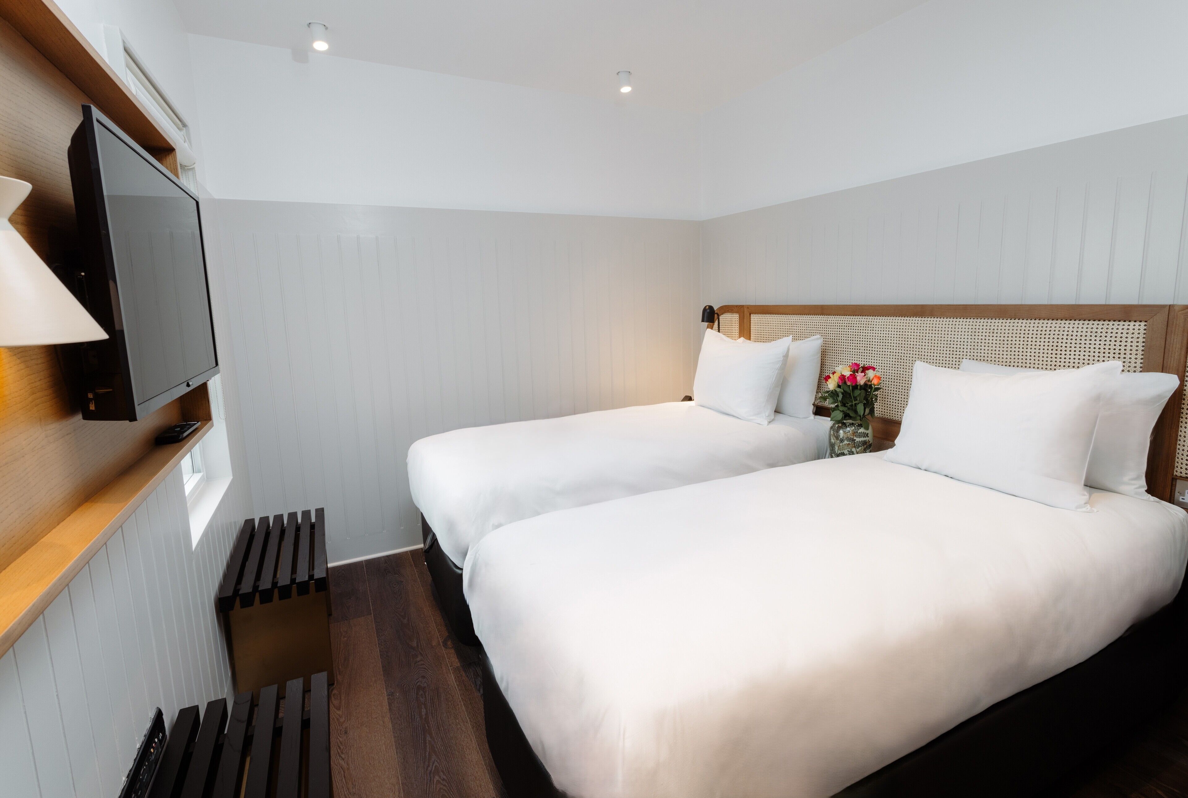 Habitación de hotel con dos camas, un televisor en un estante de madera y un ventanal pequeño.