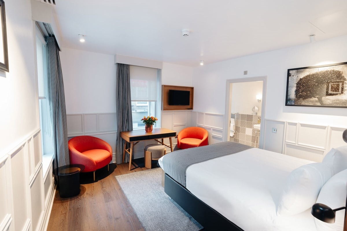 A modern hotel room with a large bed, a desk with a chair, a television, and a painting on the wall.