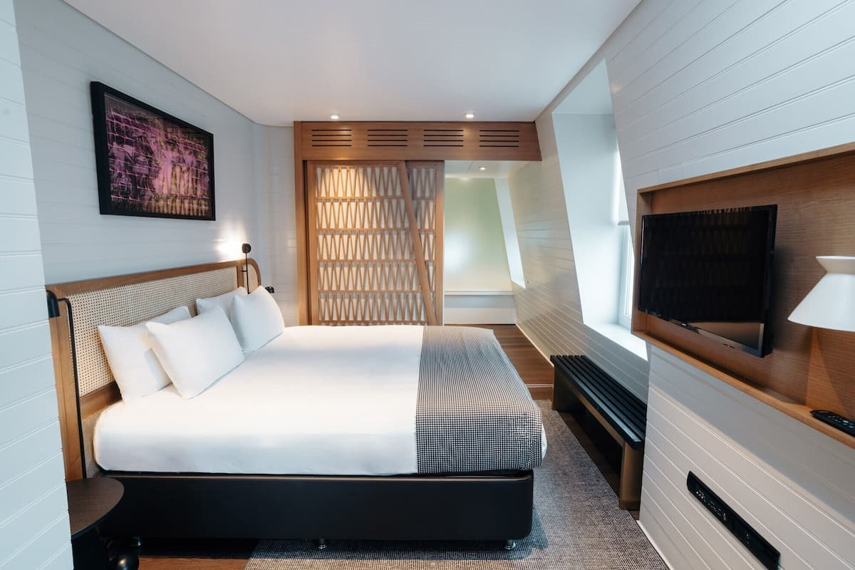A modern hotel room with a large bed, a flat-screen TV, and a wooden partition.