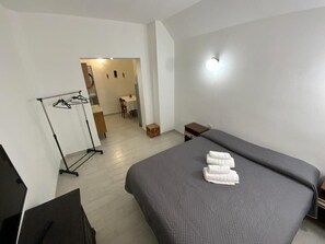 Habitación de hotel con cama, escritorio, silla, armario y baño visible a través de una puerta abierta.