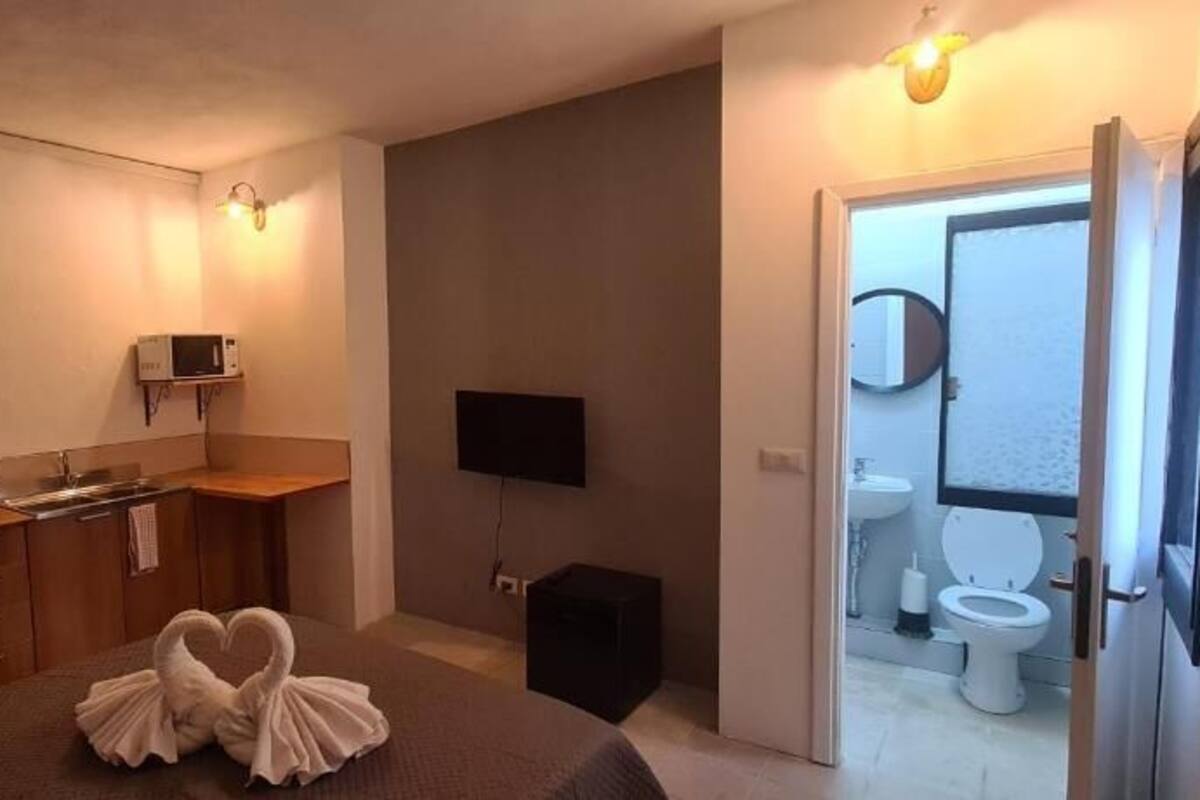 A compact room with a kitchenette, a flat-screen TV, and a door leading to a bathroom.
