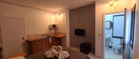 A compact room with a kitchenette, a flat-screen TV, and a door leading to a bathroom.