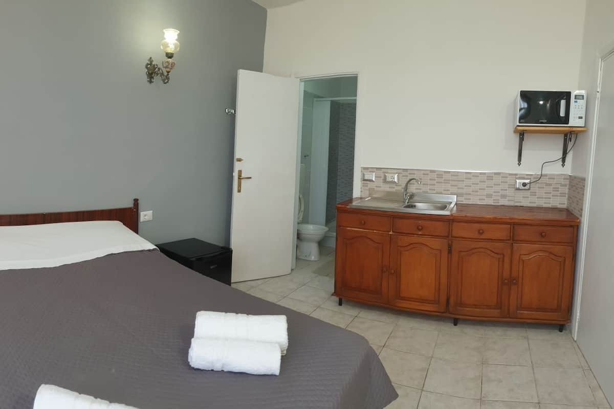 A bedroom with a bed, bedside table, and a bathroom with a sink and toilet.
