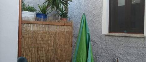 A small outdoor area with a bamboo fence, a green umbrella, and a window with a dark frame.