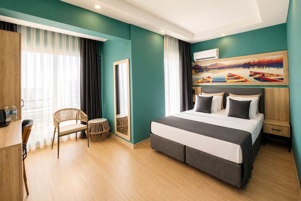 A modern hotel room with a large bed, a desk, a chair, and a painting on the wall.