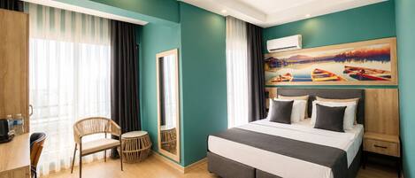 A modern hotel room with a large bed, a desk, a chair, and a painting on the wall.