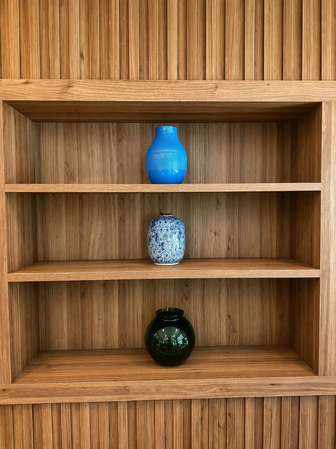 A wooden shelf unit with three shelves, each holding a different vase.