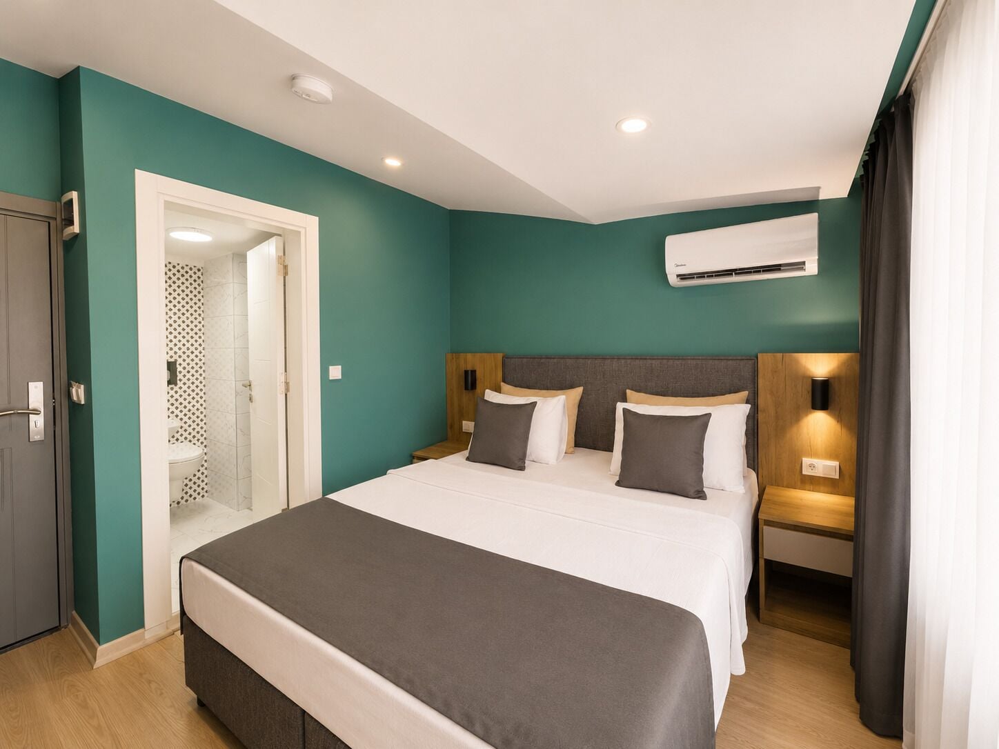 Una habitación de hotel con una cama grande, una mesita de noche con lámpara, un equipo de aire acondicionado y una puerta que da a un baño.