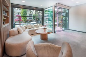 Una sala de estar moderna con un sofá seccional, una mesa de centro redonda de madera y una puerta de vidrio que da a un área exterior.