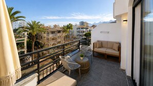Un balcón con sofá, sillas y una mesa, con vistas a un paisaje urbano con edificios y palmeras.
