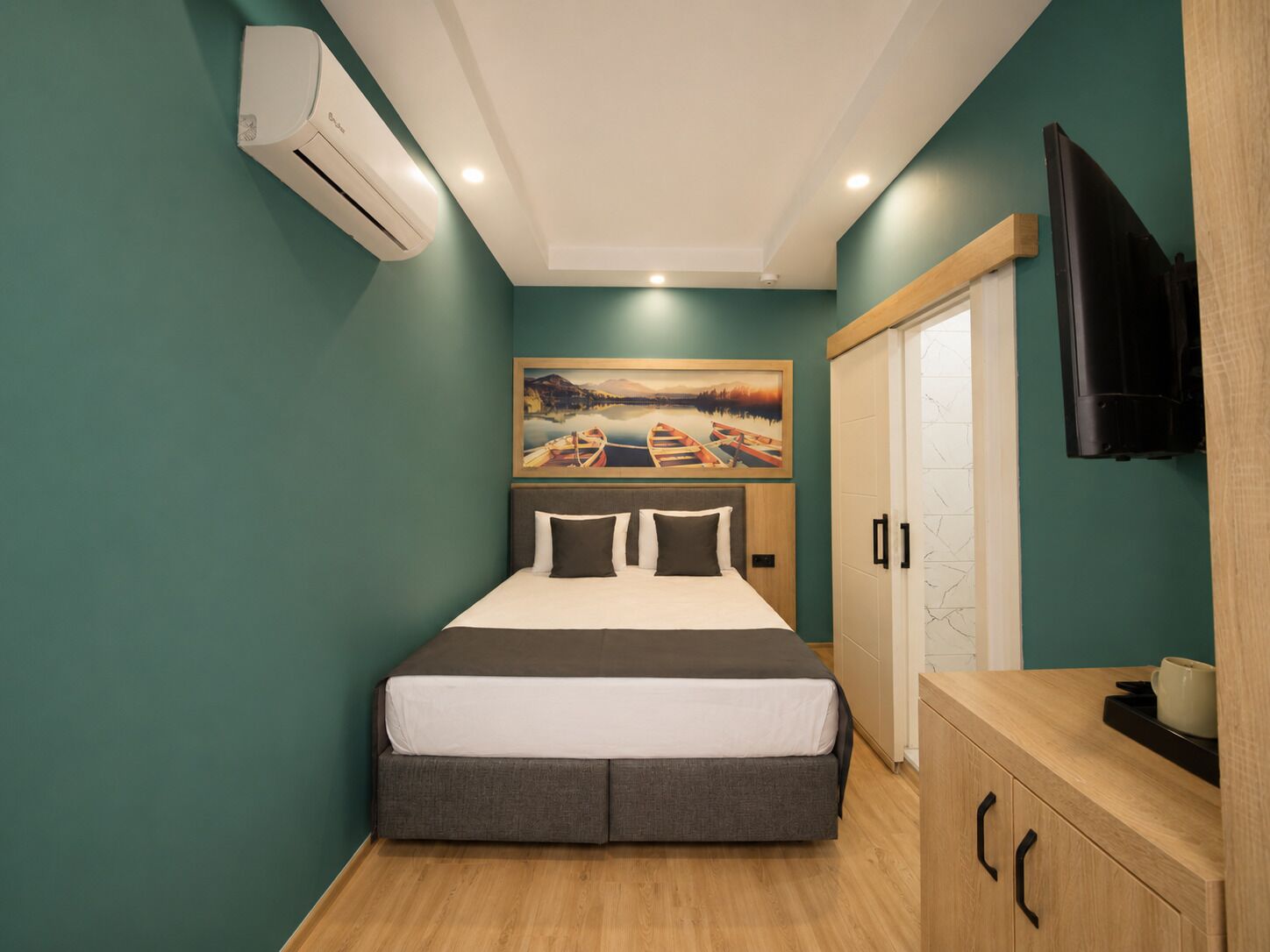 A bedroom with a bed, a painting, an air conditioning unit, a television, and a wooden cabinet.