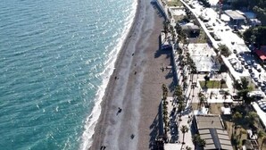 Un paisaje urbano costero con una playa extensa, edificios y una montaña al fondo.