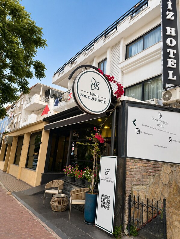A hotel sign with a logo and name, a QR code, and a small outdoor seating area with chairs and a table.