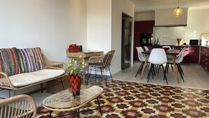 Een moderne woonkamer met een bank, stoelen, een eettafel en een keuken met kasten en apparatuur.