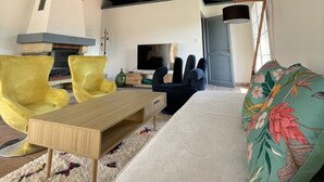Een moderne woonkamer met een hoge plafond, een open haard, een televisie en een bank met een bloemenkussen.