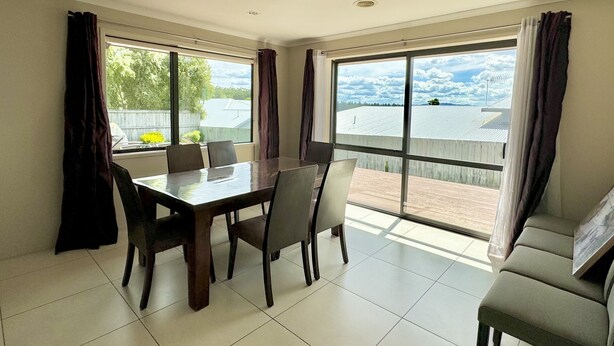 Un comedor con mesa y sillas, ventanas amplias con cortinas, y vista a un patio cercado.