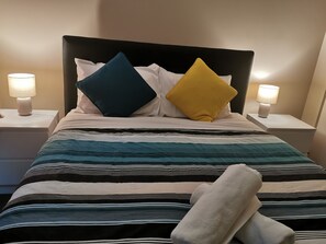A neatly made bed with striped bedding, two bedside lamps, and a headboard.
