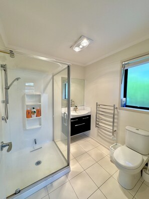 A modern bathroom with a glass-enclosed shower, a white sink, a black vanity, and a toilet.