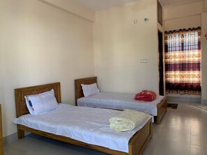 A room with two single beds, a wooden headboard, white bedding, and a curtain with a striped pattern.