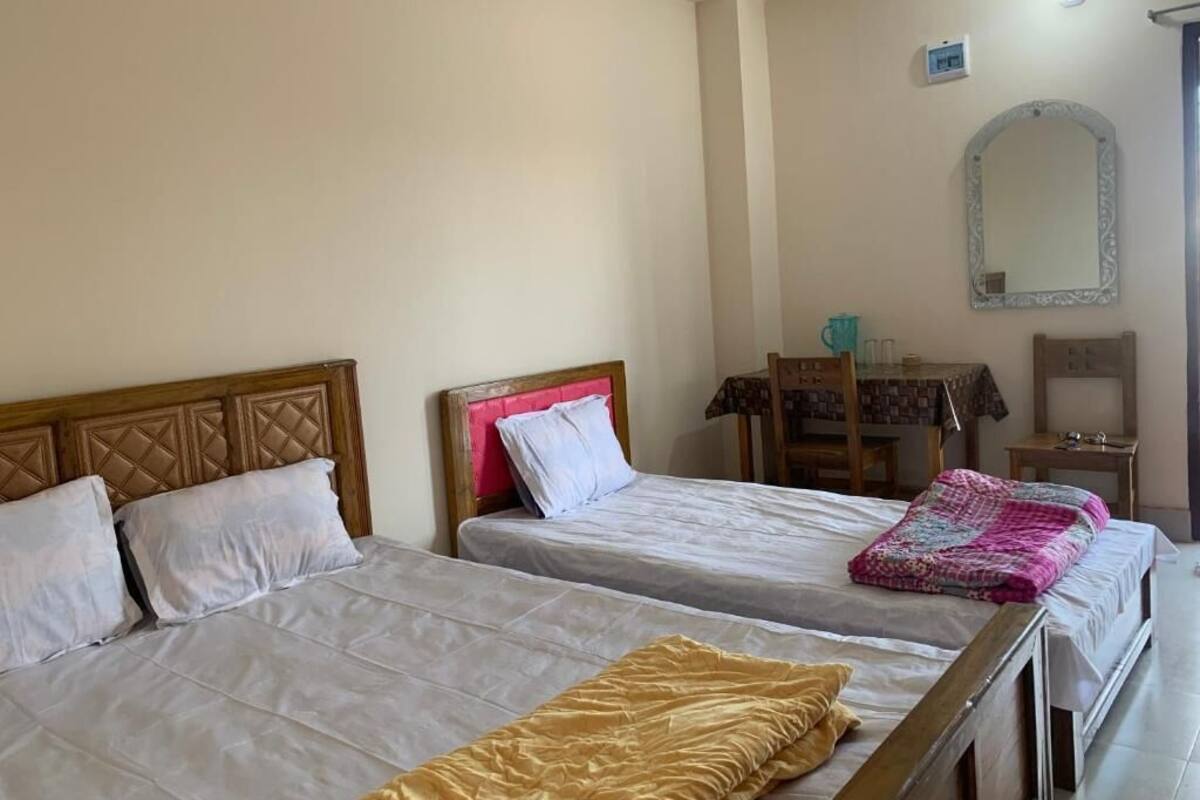 A room with three beds, a wooden headboard, a small table, and a mirror on the wall.