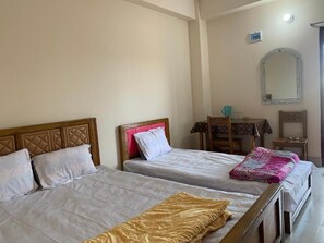 A room with three beds, a wooden headboard, a small table, and a mirror on the wall.