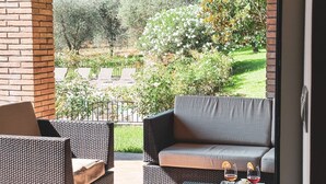 Ein Balkon mit Korbmöbeln, einer gepolsterten Couch und zwei Weingläsern auf einem Tablett.