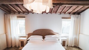Ein Schlafzimmer mit Holzbalkendecke, einem großen Bett mit weißer Bettwäsche, zwei Nachttischen und einem Fenster mit Vorhängen.