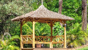 Un belvédère en bambou, doté d’un toit de chaume, entouré d’une végétation luxuriante et d’arbres.