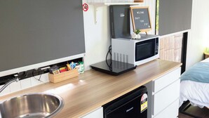 Une petite cuisine équipée d’un évier, d’un four à micro-ondes, d’un petit réfrigérateur et d’une étagère avec des verres et un panneau.