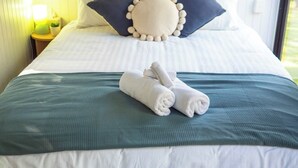 Un lit bien fait, recouvert d’une couverture verte, avec deux serviettes enroulées et des coussins décoratifs ornés de pompons.