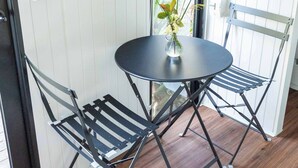 Une table ronde surmontée d’un vase de fleurs, deux chaises noires pliantes et un plancher en bois.