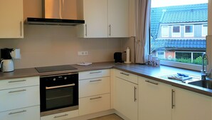 A modern kitchen with white cabinets, a built-in oven, a range hood, and a window with a view of a blue-roofed building. - fewo1846 - Kranich Museumsberg - apartment with 2 bedrooms on the ground floor (Flensburg)