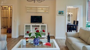 A living room with a chandelier, a TV on a white cabinet, a vase with roses, and a dining area with a table and chairs. - fewo1846 - Kranich Museumsberg - apartment with 2 bedrooms on the ground floor (Flensburg)