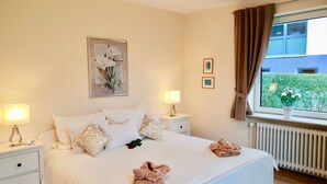 A hotel room with a bed, two bedside tables with lamps, a window with curtains, and a radiator. - fewo1846 - Kranich Museumsberg - apartment with 2 bedrooms on the ground floor (Flensburg)