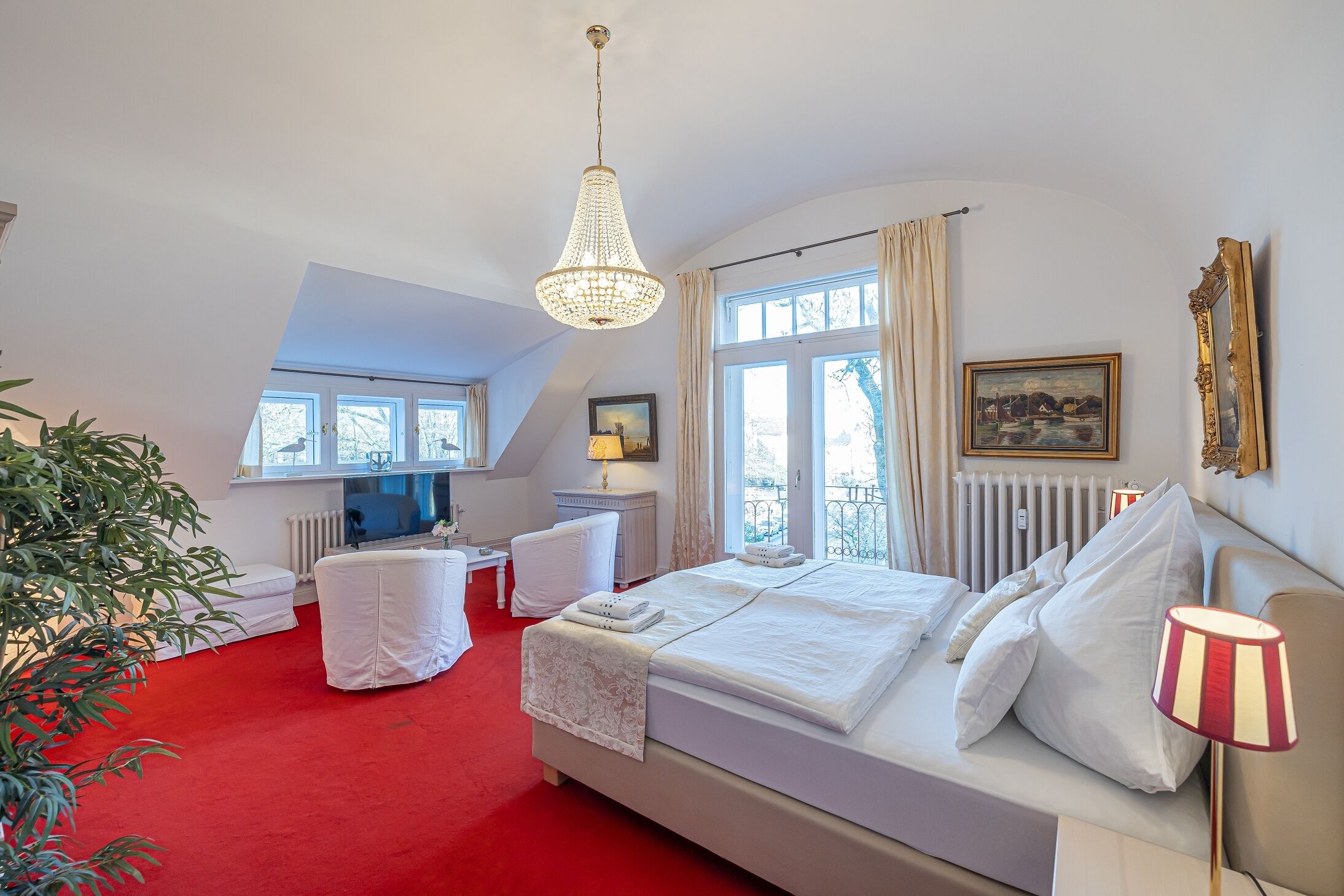 A bedroom with a large bed, a desk, a chair, a radiator, and a window.